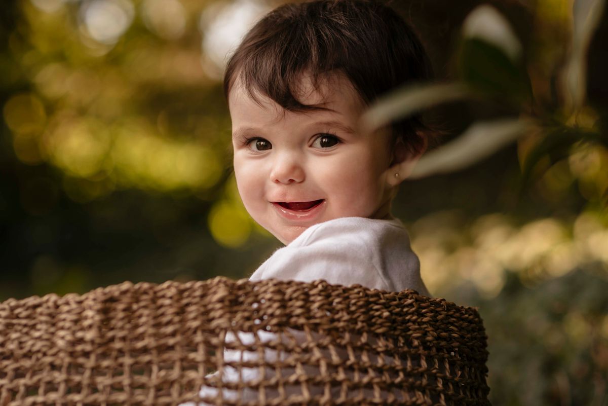 Smiling baby sitting outdoors in a woven basket surrounded by nature