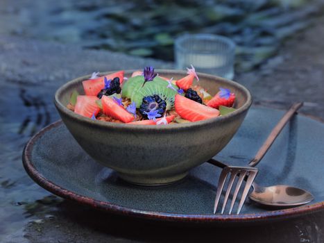 A visually appealing fruit salad topped with edible flowers in a ceramic bowl. Ideal for gourmet presentations.