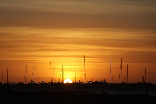 Free Silhouetted sailboats set against a dramatic sunset sky at a tranquil harbor. Stock Photo