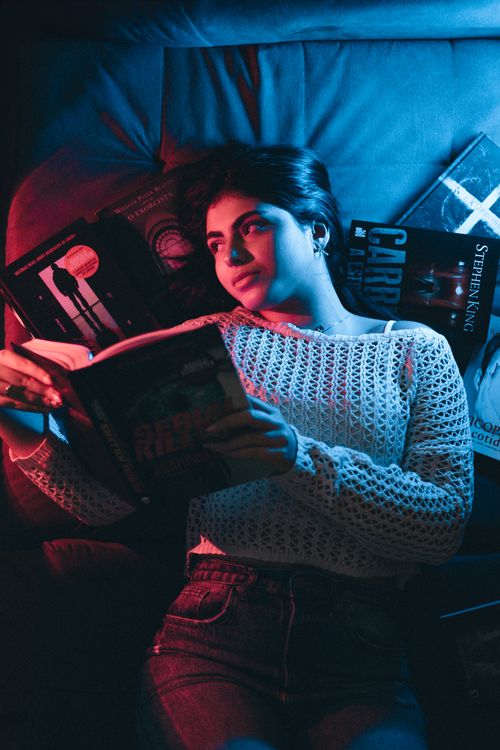 Free Young woman reading a book under dramatic neon lighting, creating a moody ambiance. Stock Photo