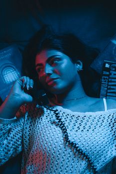 Young woman in moody lighting talking on landline phone, surrounded by books.