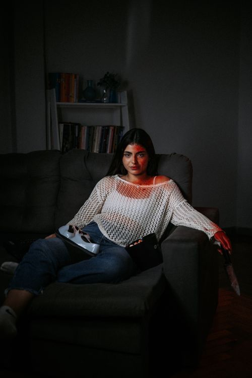Free Woman relaxing on a couch in a dimly lit room with moody lighting. Stock Photo