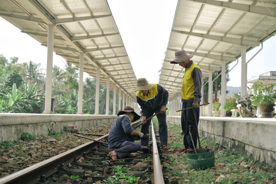 Three workers repairing railway tracks at a rural station during the day. Three workers repairing railway tracks at a rural station during the day.
