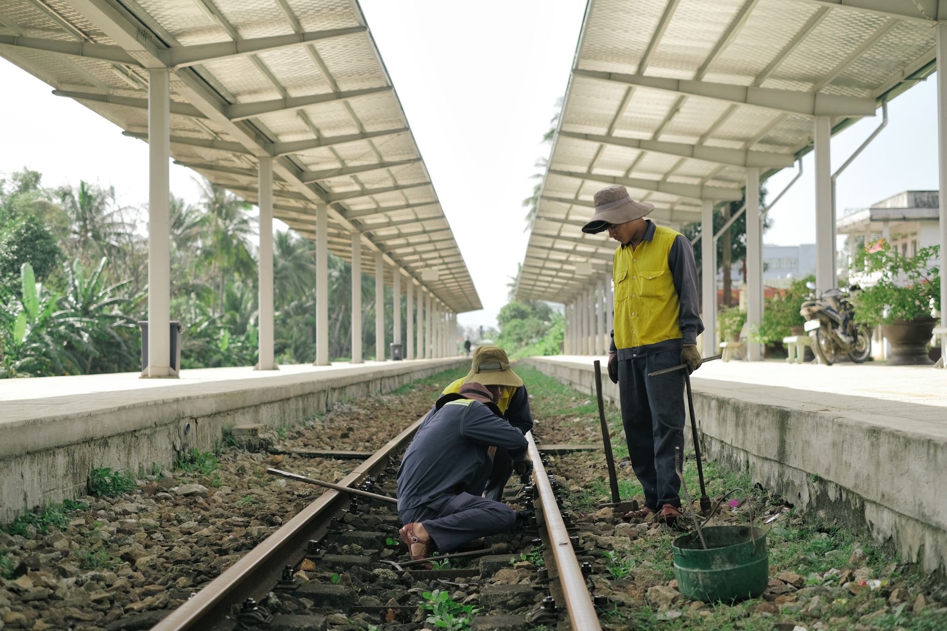 Workers wearing yellow safety vests inspect railway tracks at an outdoor station.