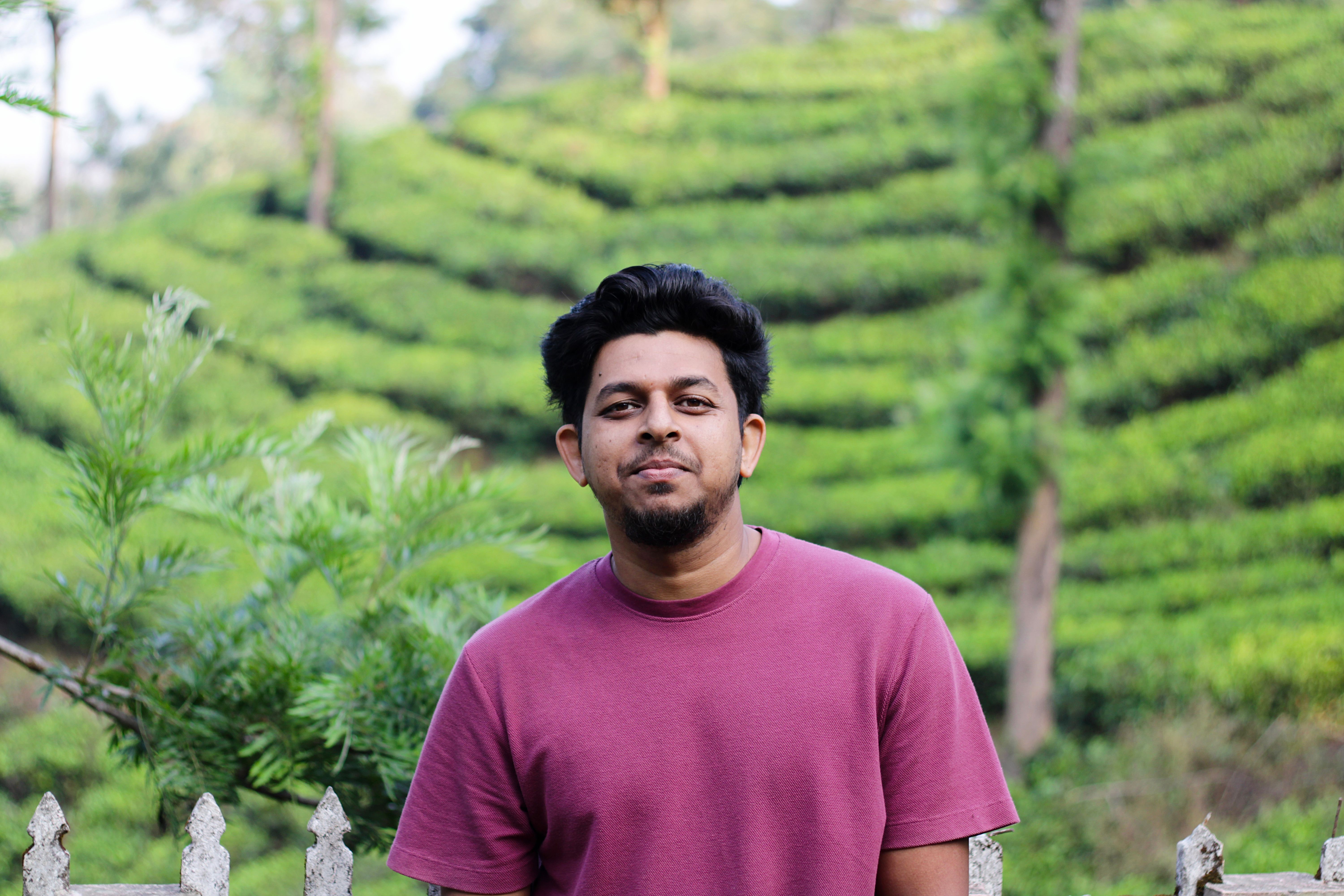 A man stands smiling in front of lush green tea plantations in Nadukani, Kerala.