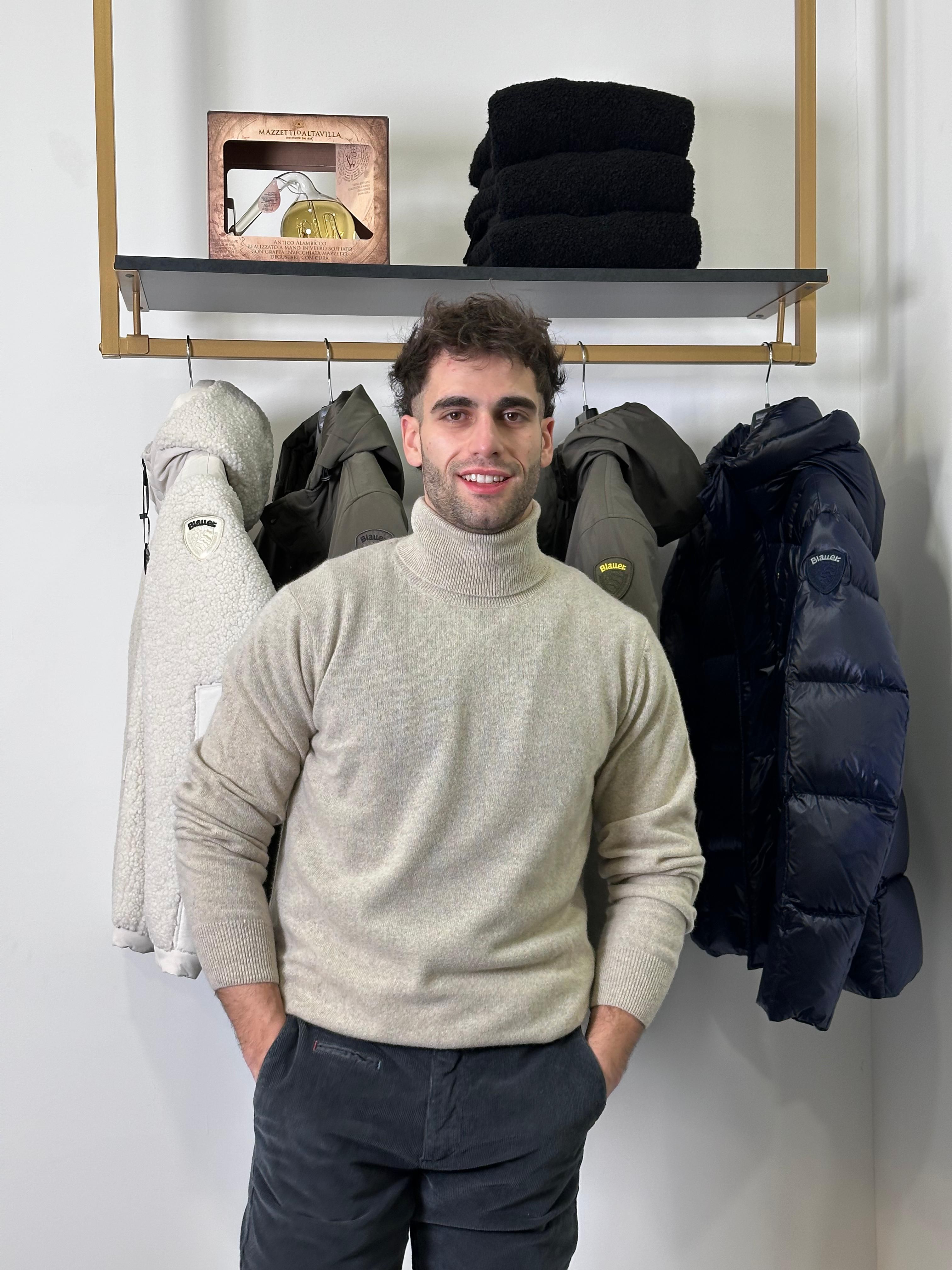 Portrait of a young man in a turtleneck standing in a fashion clothing store with jackets.