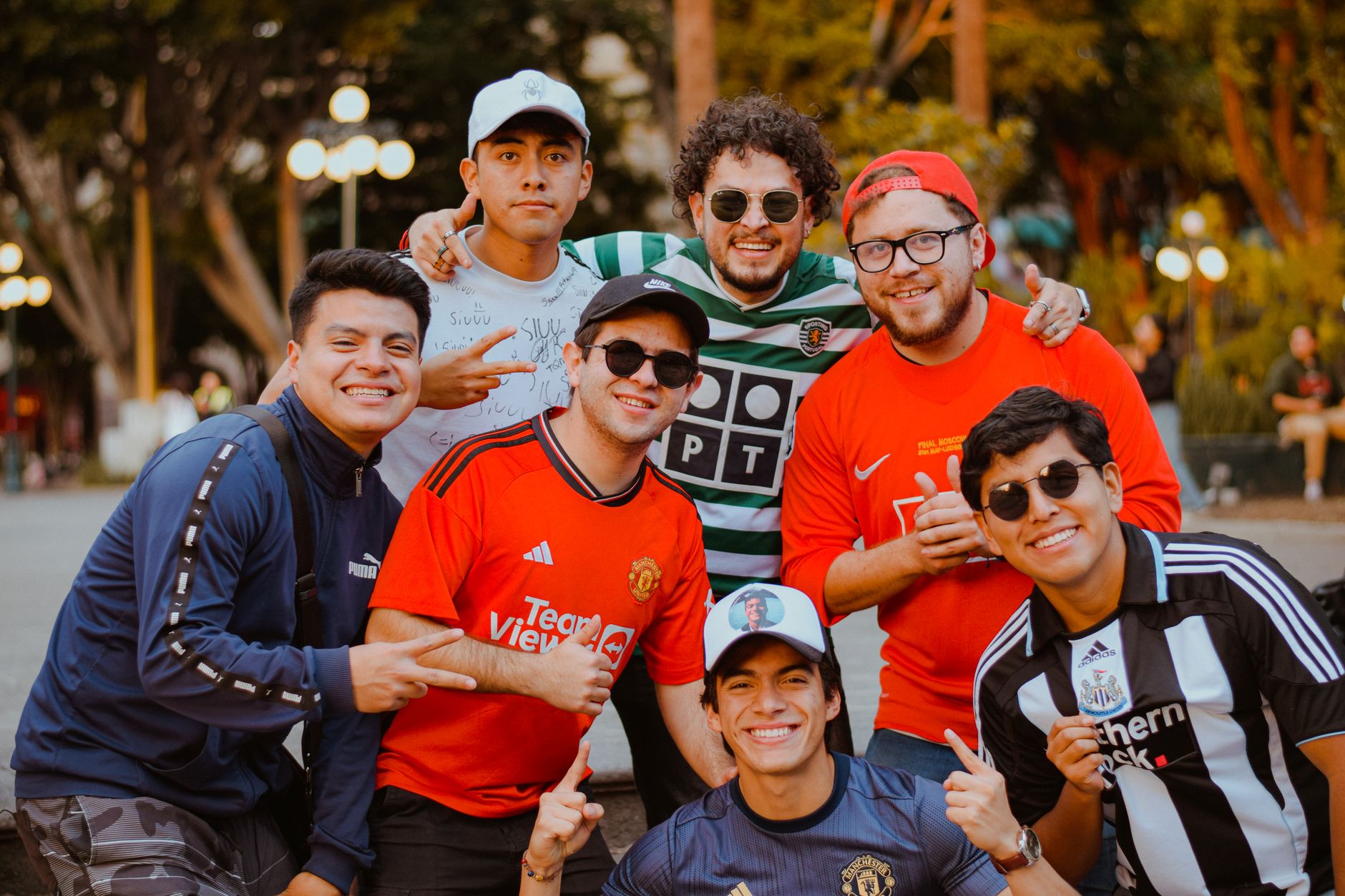 A cheerful group of young adults in soccer jerseys posing outdoors on a sunny day.