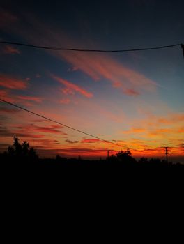 Capture the beauty of a vivid sunset with silhouetted trees and overhead power lines, showcasing nature's colorful transition at twilight.