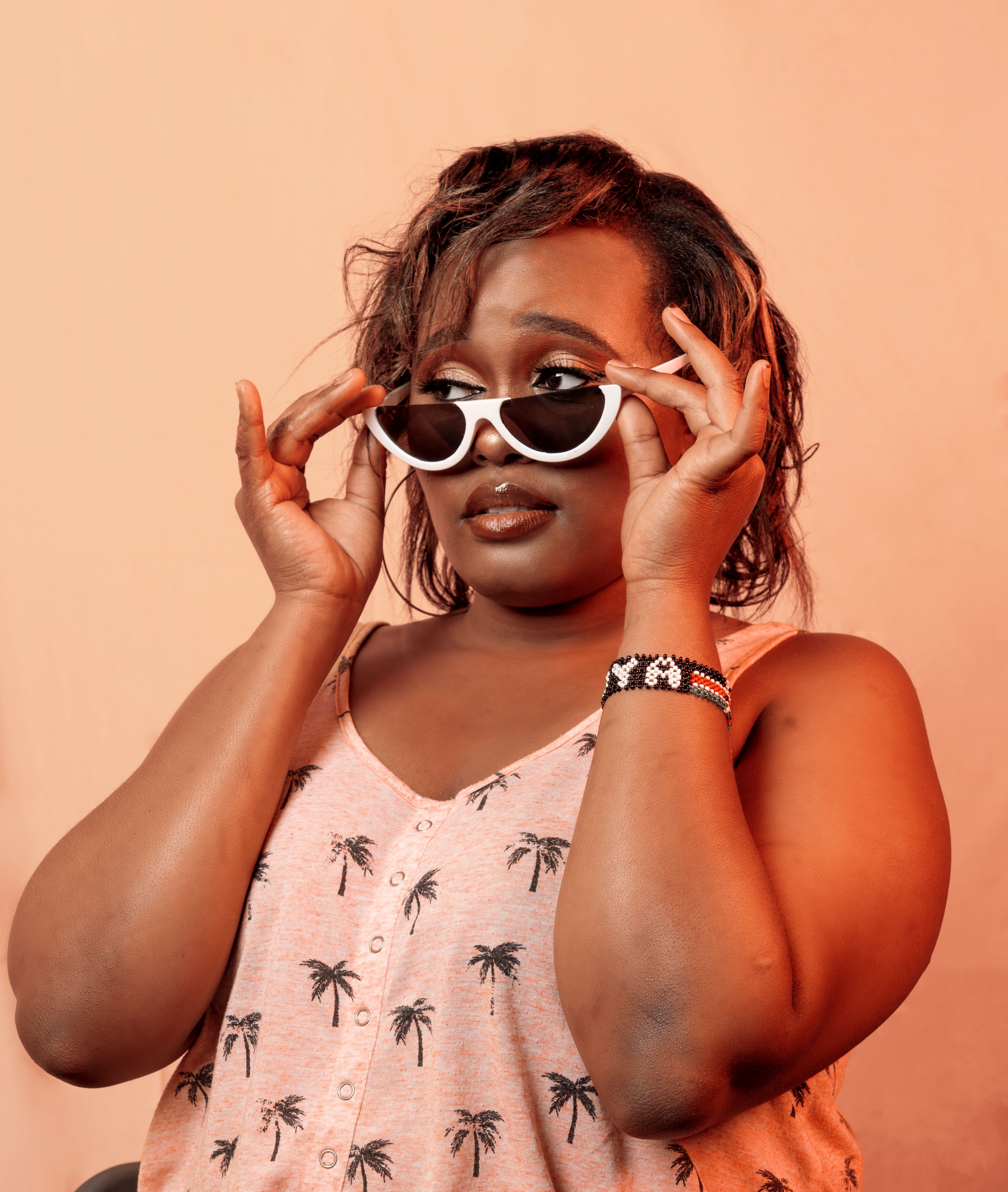 Fashionable woman wearing palm print top and retro sunglasses in studio portrait.