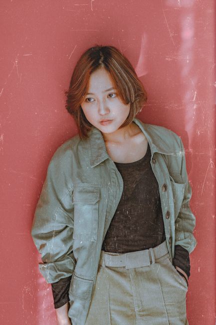 Elegant woman in fashionable outfit poses against a textured wall.