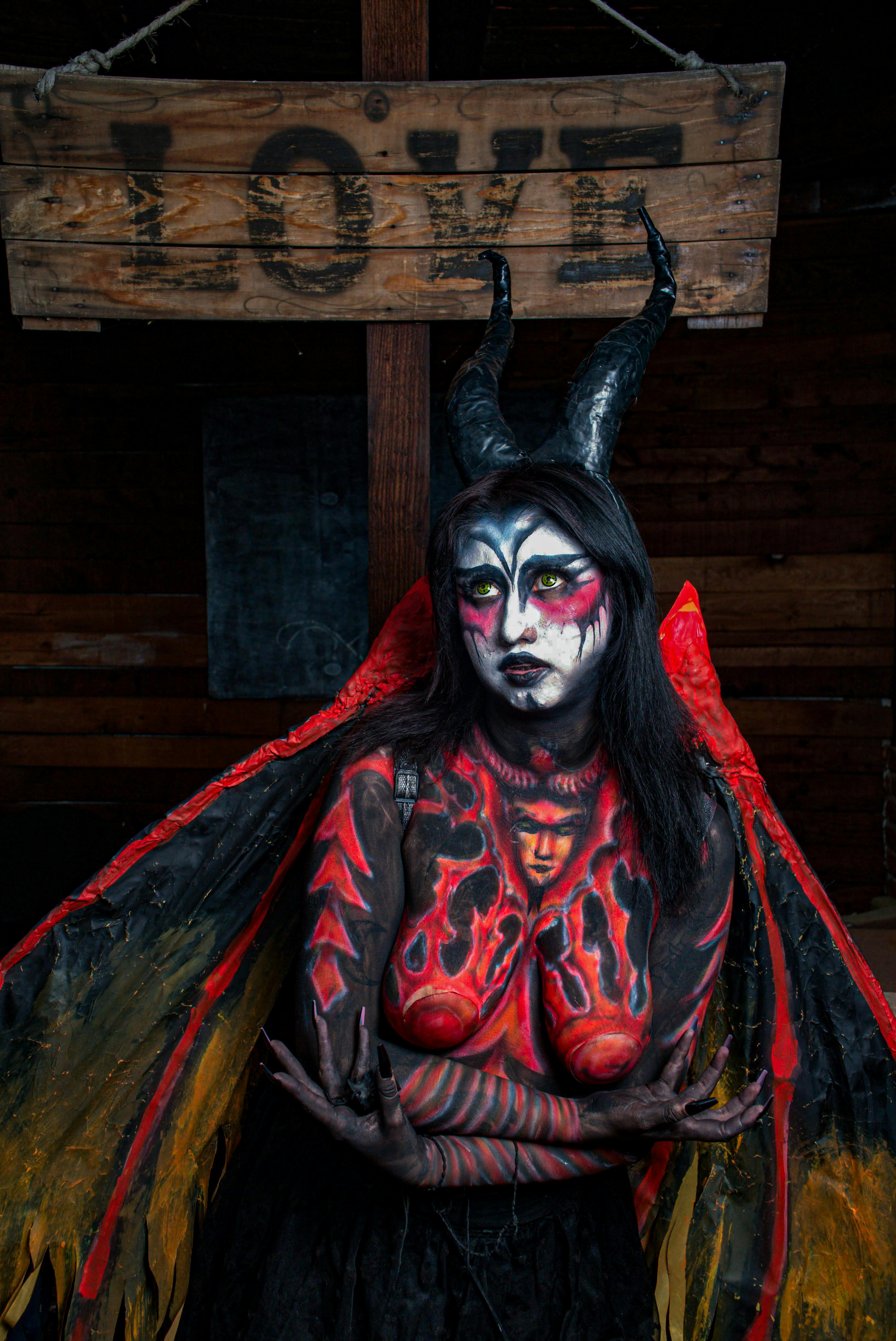 Ücretsiz Sanatsal vücut boyası ve boynuzları olan bir karakter, karanlık bir fantezi sahnesi yaratmak için 'AŞK' tabelasının altında duruyor. Stok Fotoğraflar