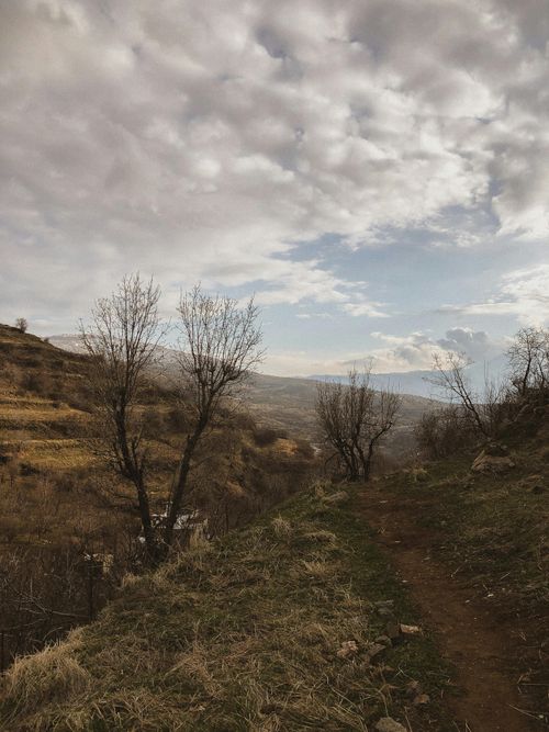 Free A tranquil dirt path winds through a barren hillside under a cloudy sky. Stock Photo