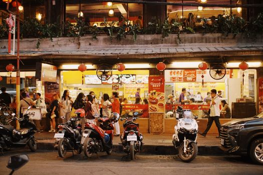 Bustling street food market scene with people enjoying local Asian cuisine at night.