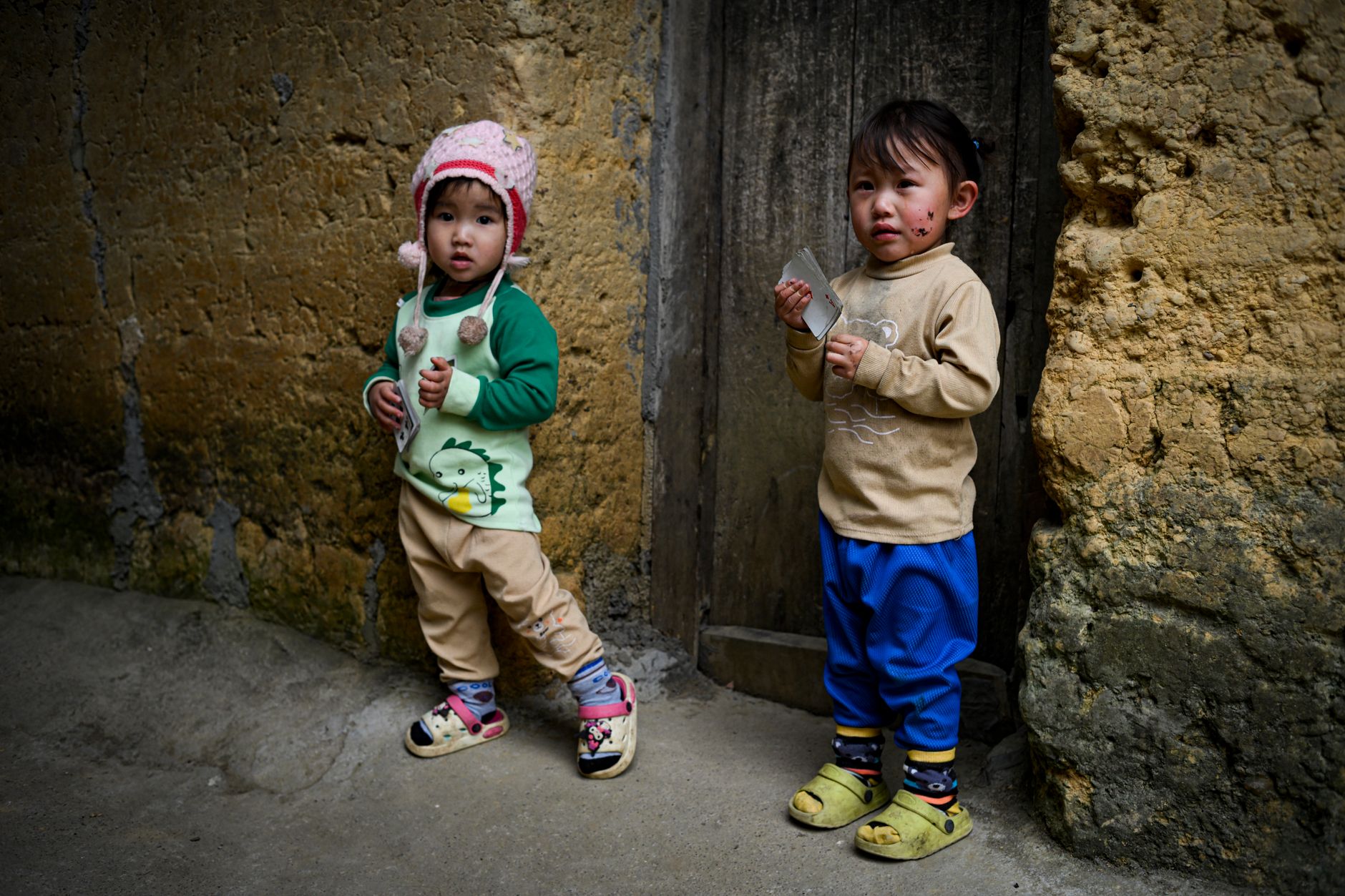 Two young children in a rustic Vietnamese setting, reflecting local culture.