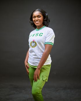 Young woman in NYSC uniform confidently posing indoors with a smile.