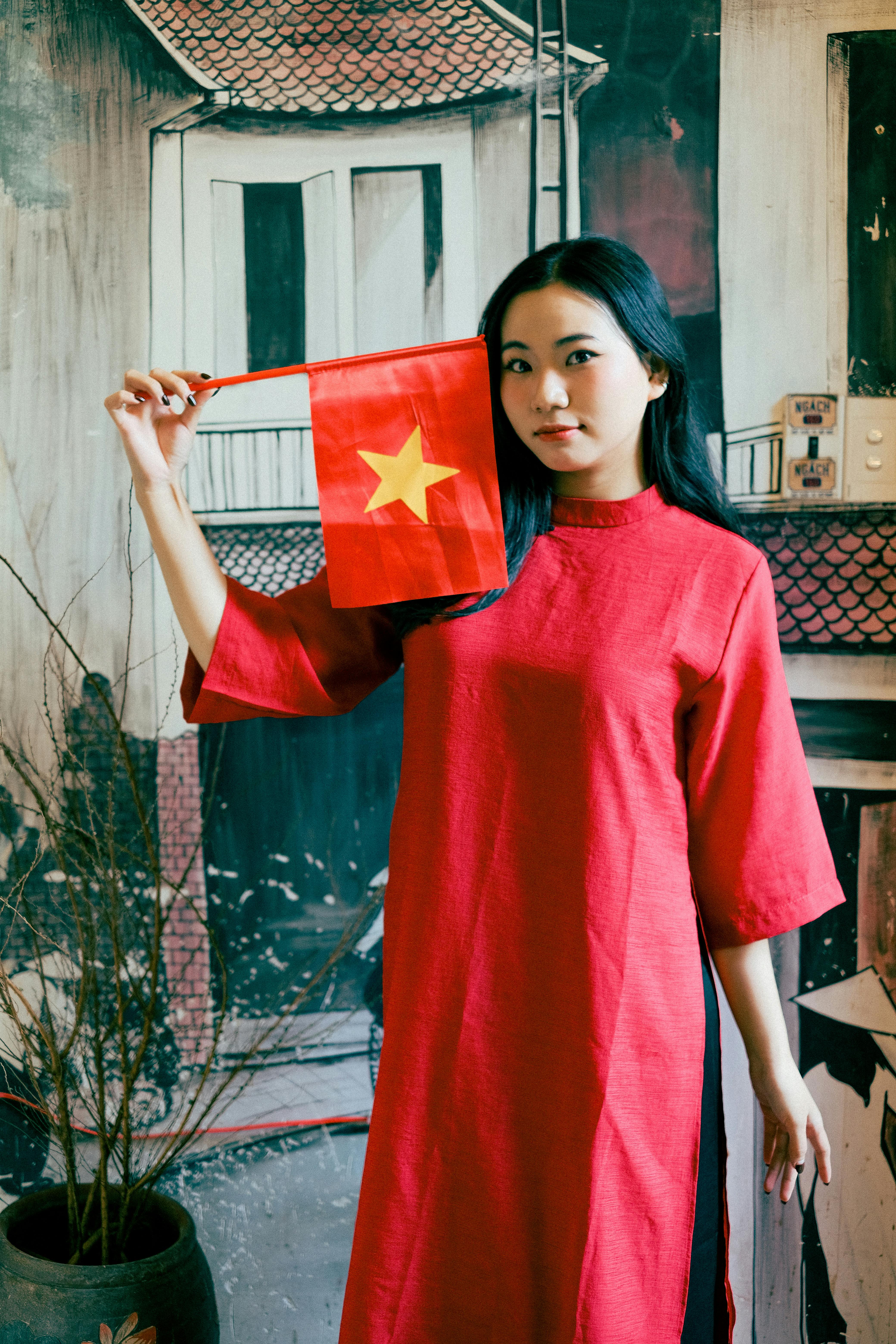 Woman in traditional red dress holding Vietnam flag indoors. Artistic background.