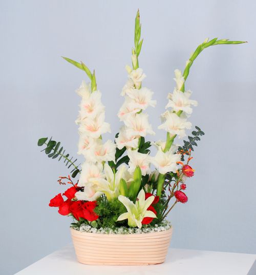 Free A beautiful bouquet featuring white gladiolus, lilies, and red roses in a modern vase. Stock Photo