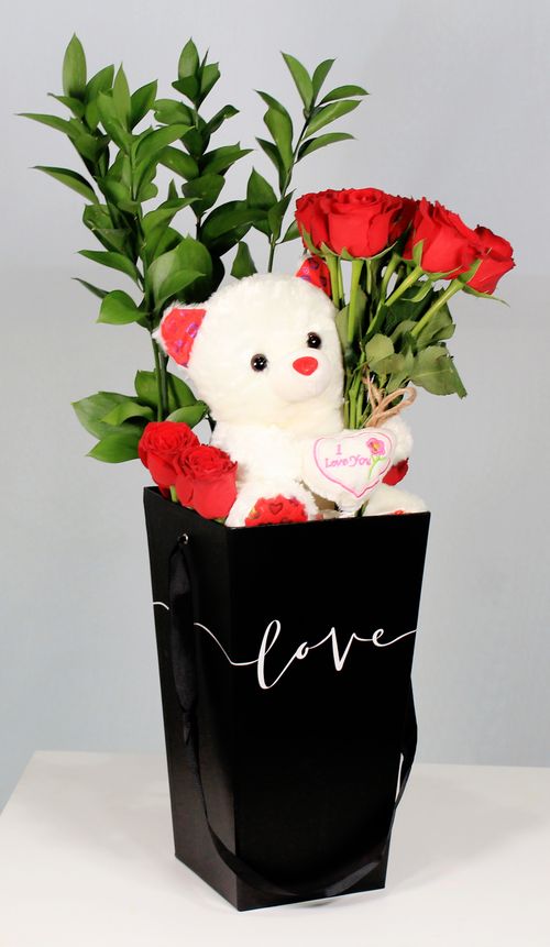 Free A charming floral arrangement with roses and teddy bear in a gift bag labeled 'love', perfect for romantic occasions. Stock Photo
