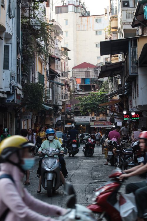Free A lively street in Hanoi's Old Quarter with scooters and pedestrians amidst narrow buildings. Stock Photo