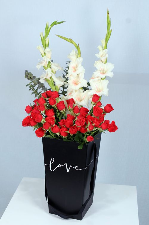 Free A stunning bouquet featuring red roses and white gladiolus in a black vase with 'love' inscription. Stock Photo