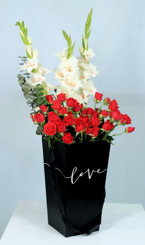 Free A stylish bouquet of red roses and white gladiolus in a black bag with 'love' sign. Stock Photo