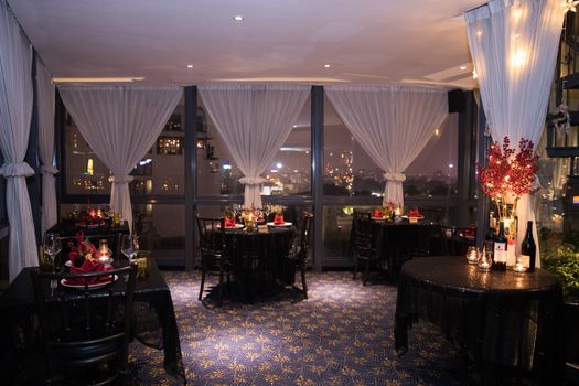 Cozy restaurant interior with cityscape view, elegant dining setup at night.