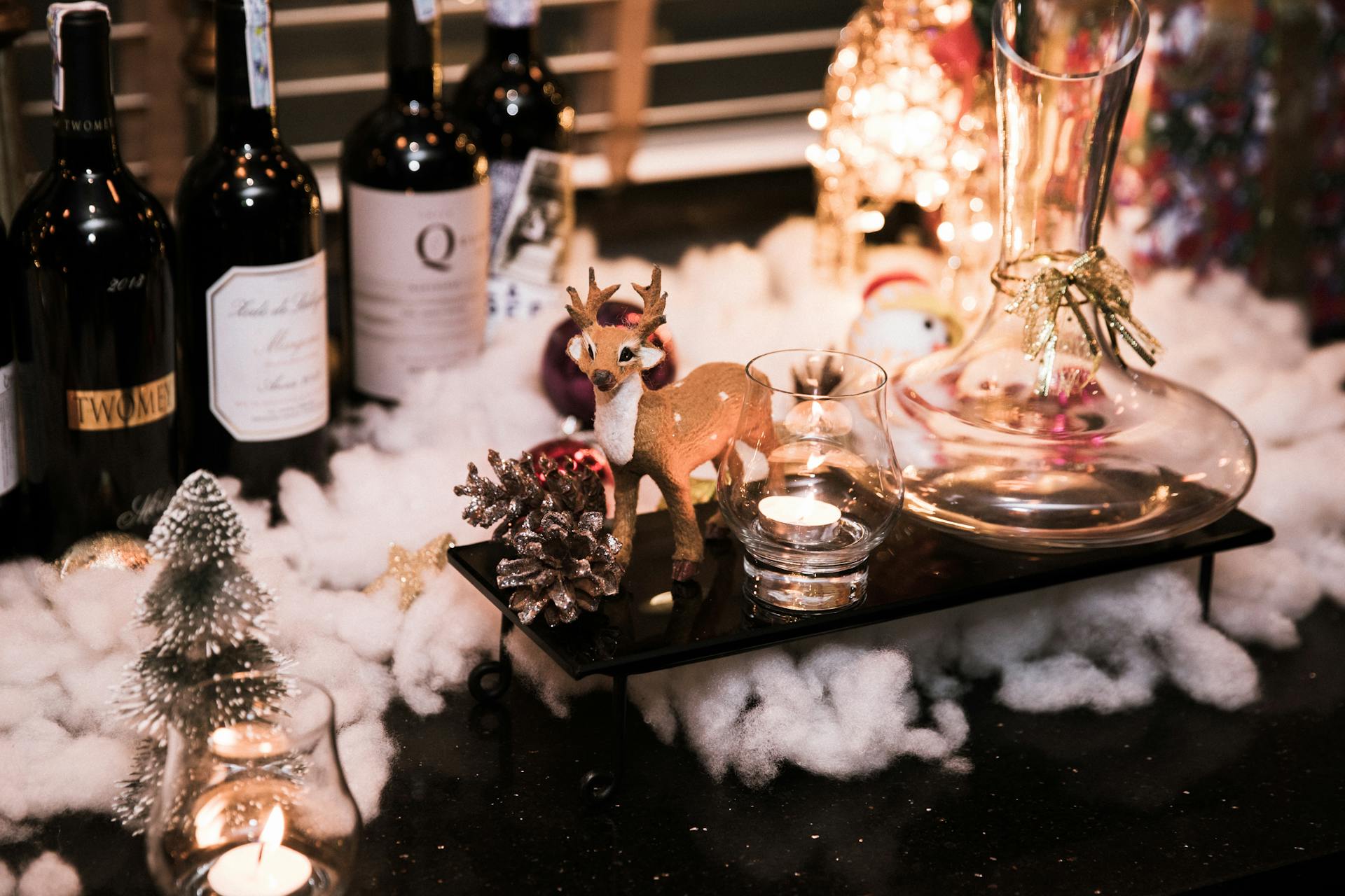 A cozy holiday scene featuring wine bottles and festive Christmas decor, including a reindeer and lit candle.