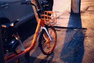 黄昏时分，一辆亮橙色的自行车停在城市街道上，潮湿的人行道上映着它的倒影