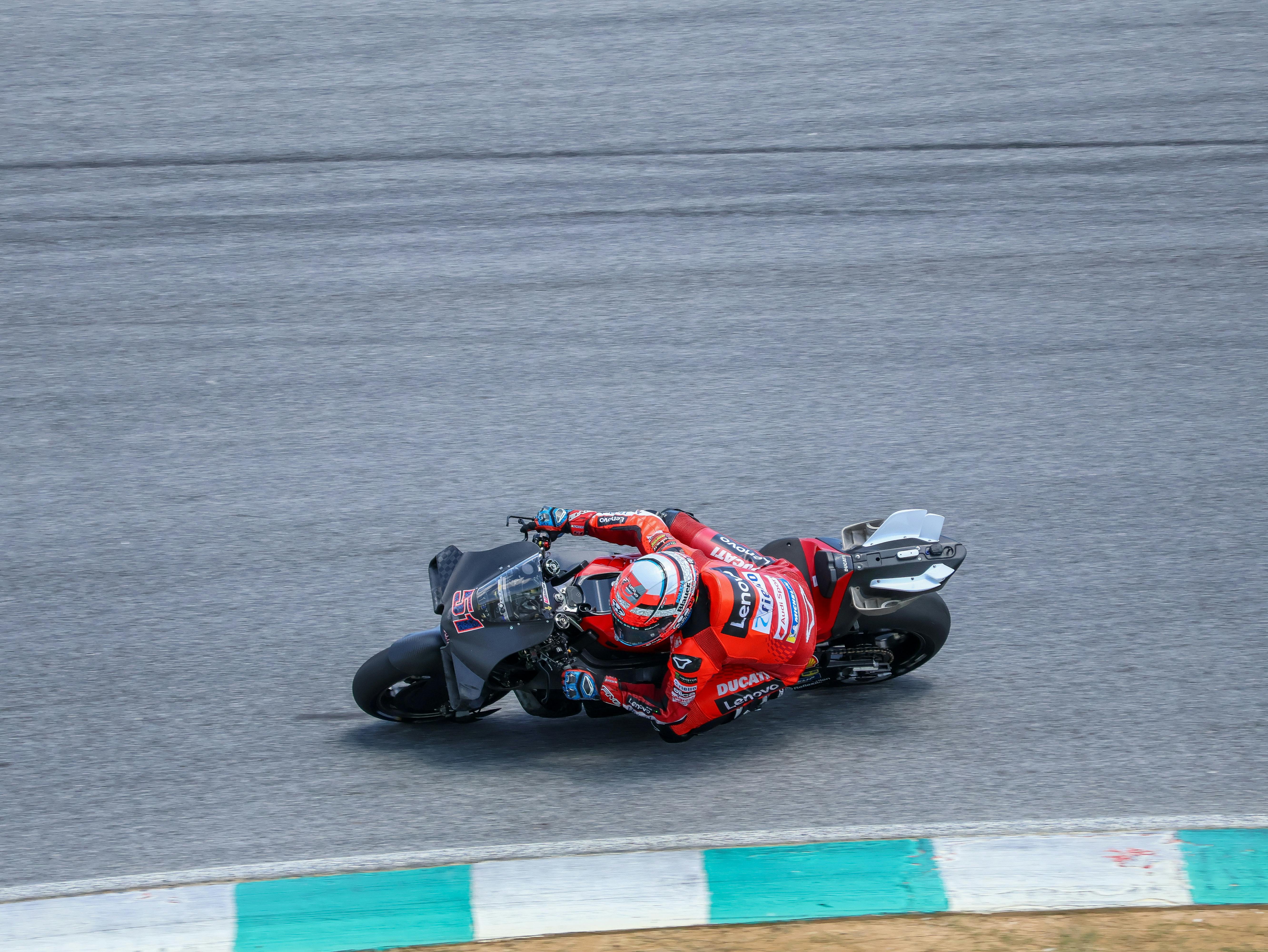 Ducati motorcycle racing on track with rider in red gear, capturing high-speed action.