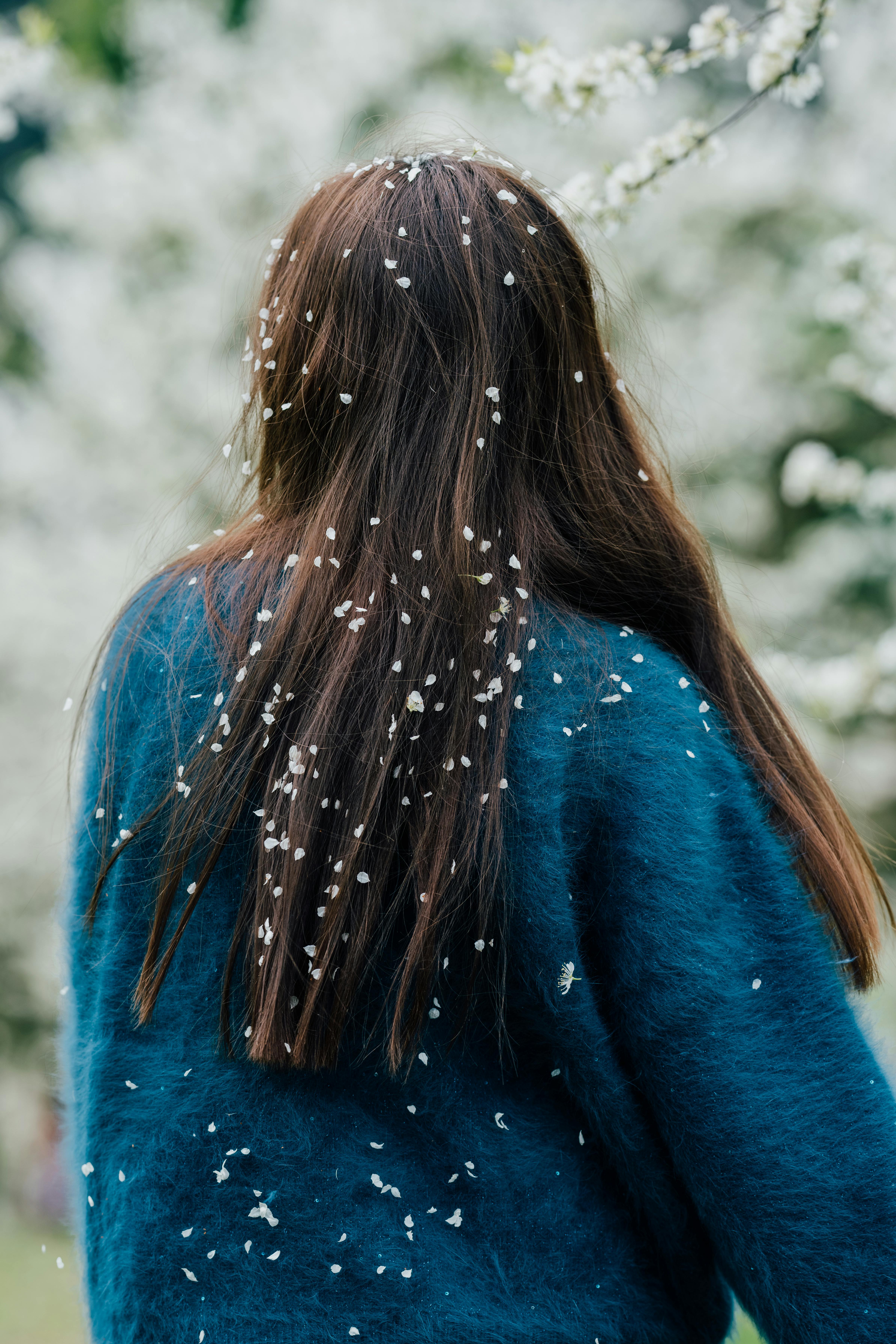 A young woman with flower petals in her hair in a blossoming spring garden.
