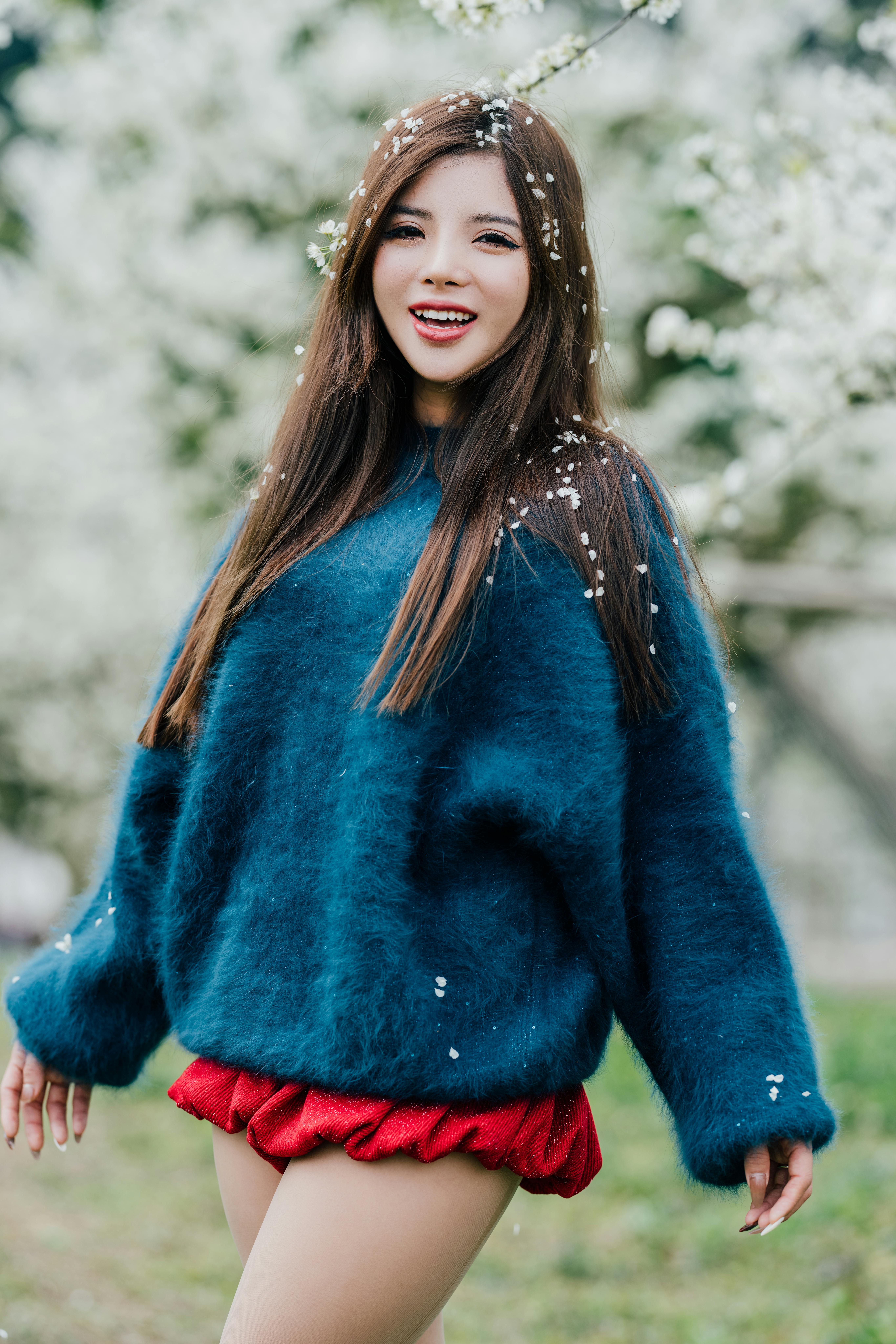 Joyful woman in a blue sweater surrounded by spring blossoms, capturing a moment of happiness.
