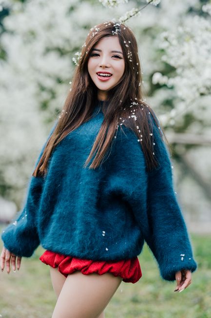 Joyful woman in a blue sweater surrounded by spring blossoms, capturing a moment of happiness.