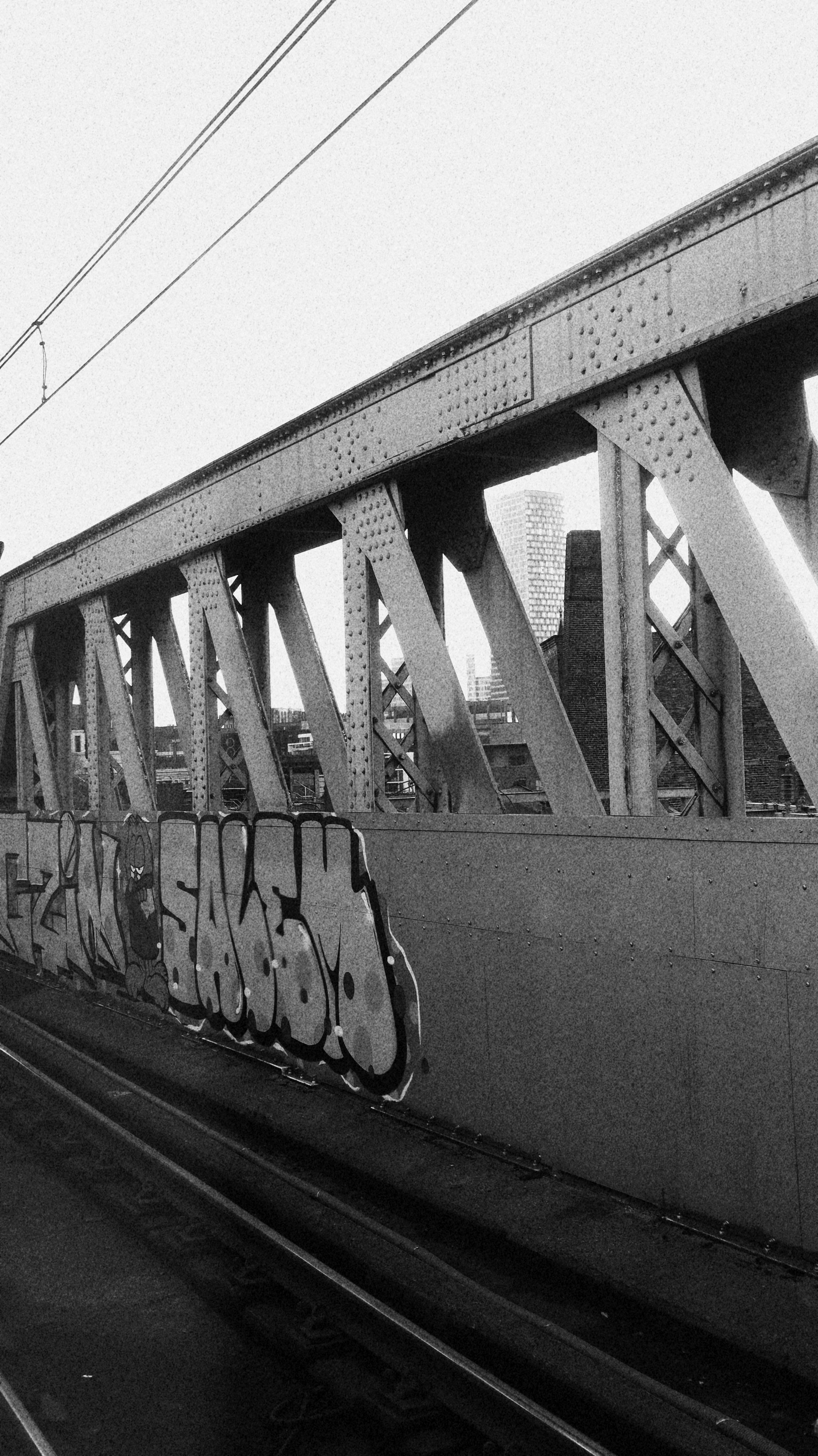 Black and white photo of graffiti on a city bridge with urban landscape in the background.