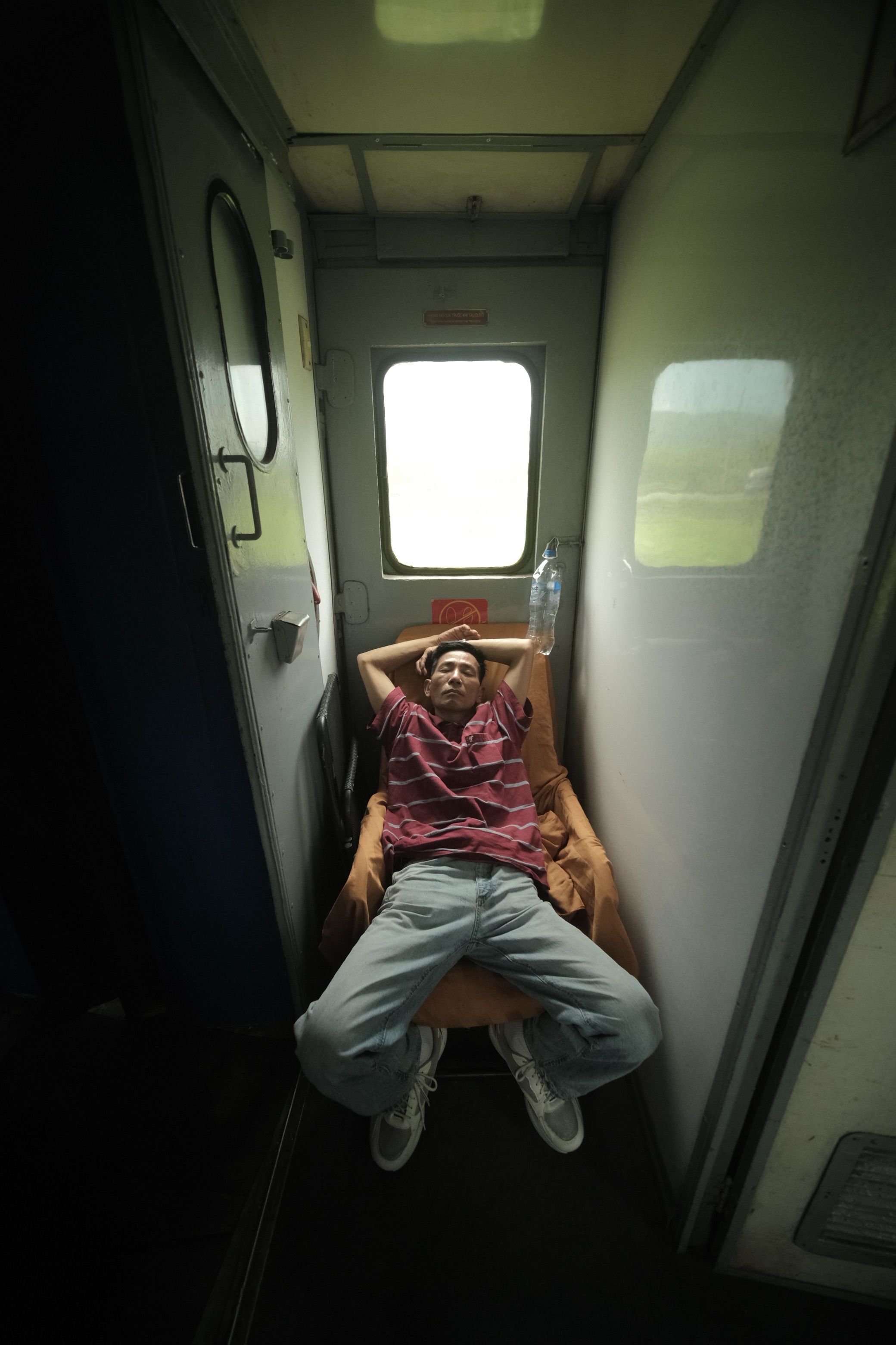 A man in casual attire relaxes in a train corridor, capturing a travel moment.