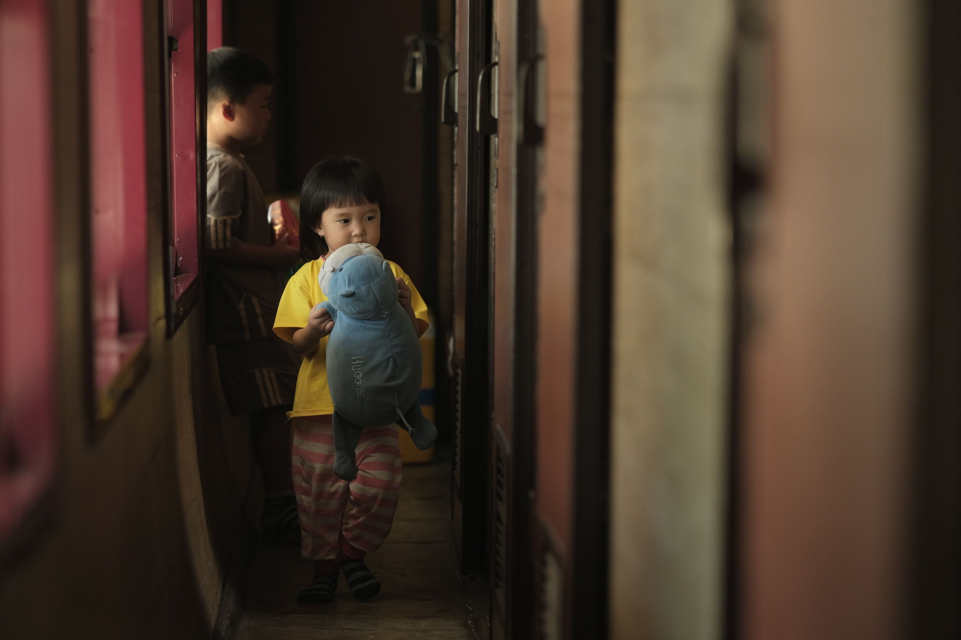 A young child holding a plush toy in a dimly lit train corridor, capturing a moment of innocence and travel.