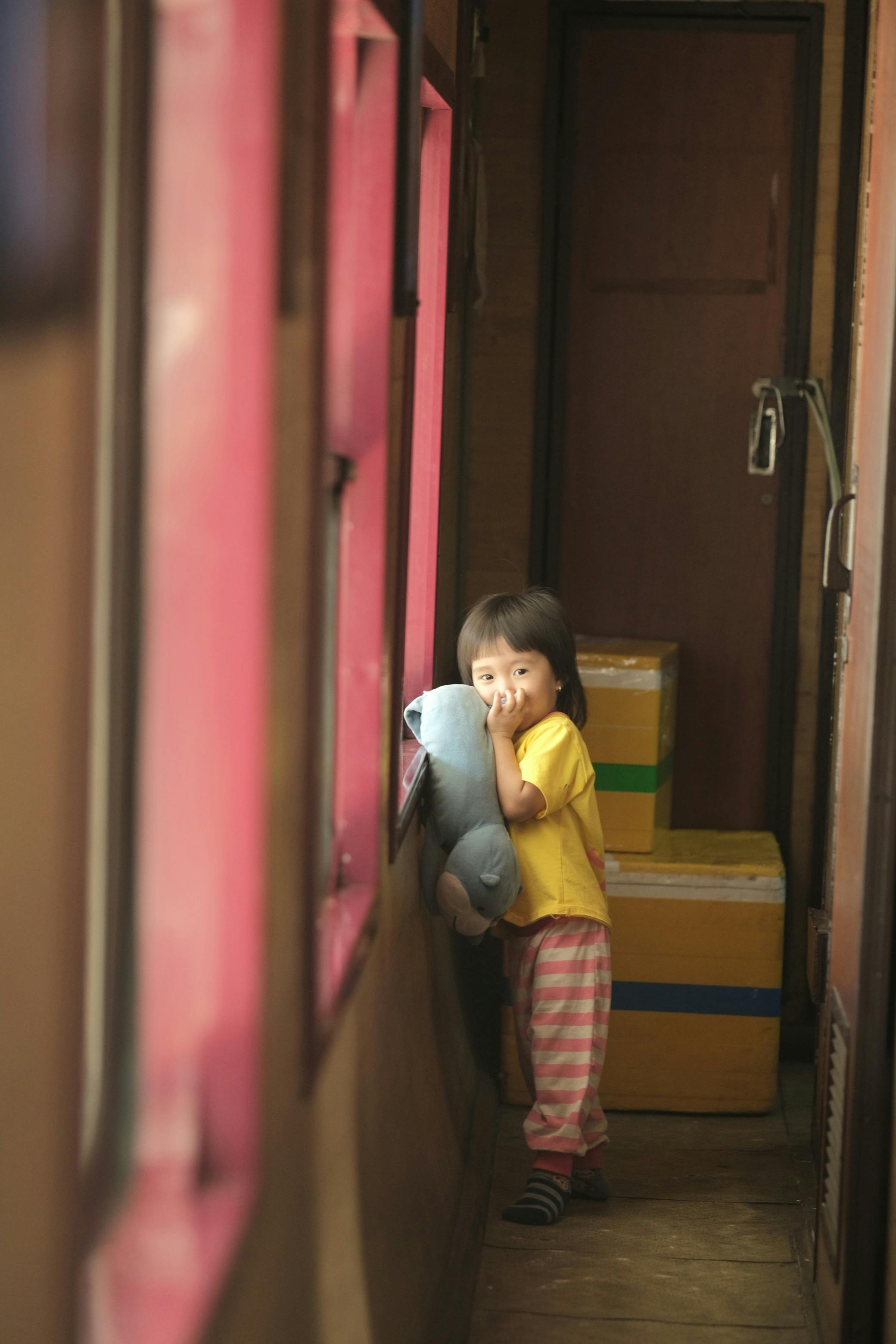 A young child gazes out a train window while holding a teddy bear, creating a nostalgic moment.
