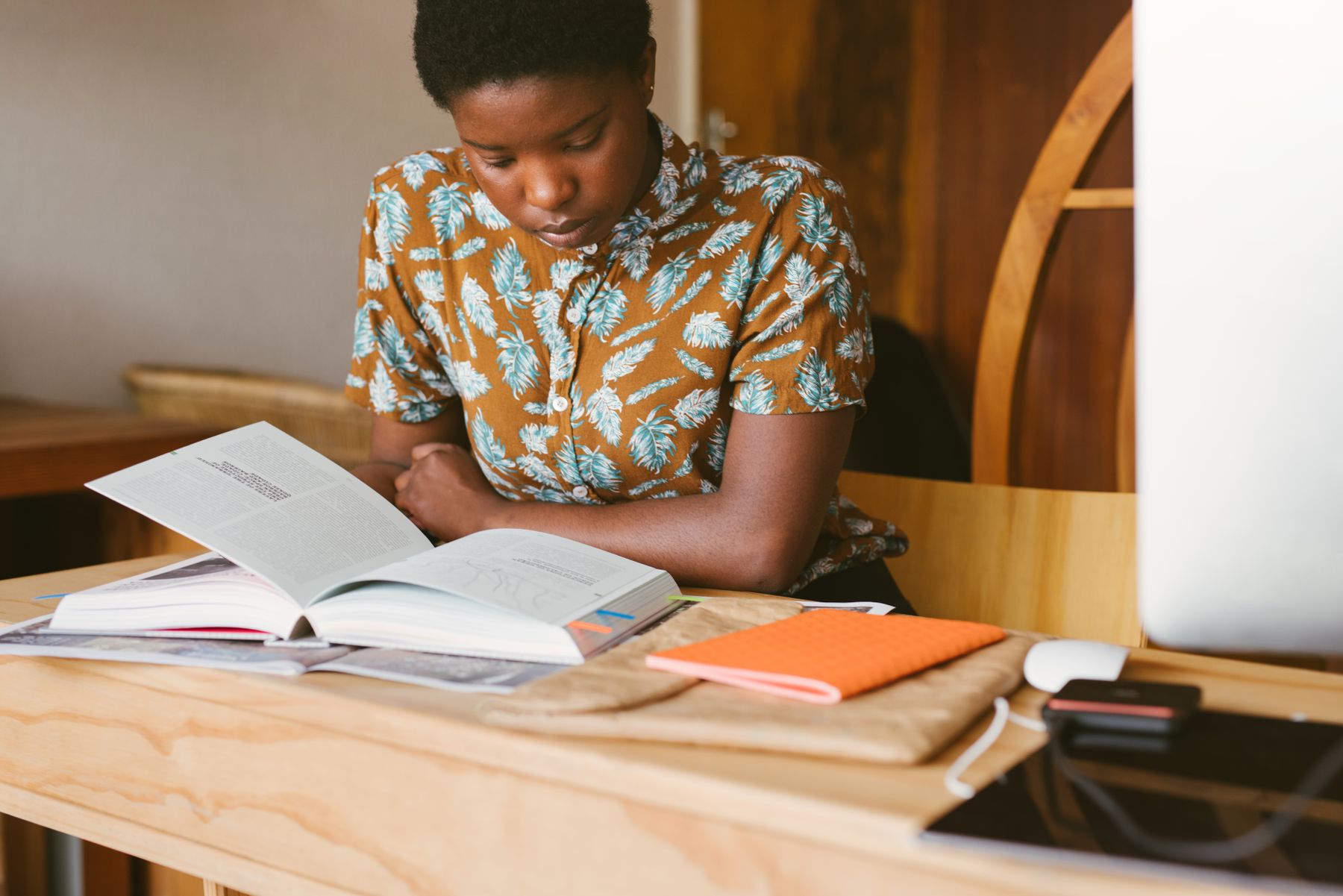 A woman writing plans in a paper notebook at a warm wooden table