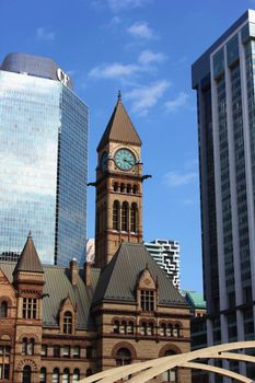 Toronto's Old City Hall with modern skyscrapers and blue sky in view.