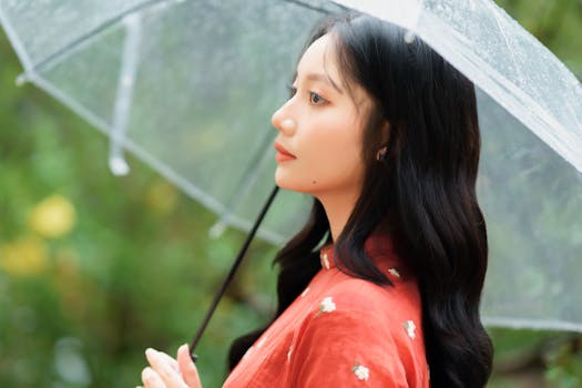 Elegant woman holding a transparent umbrella in a serene rainy setting.