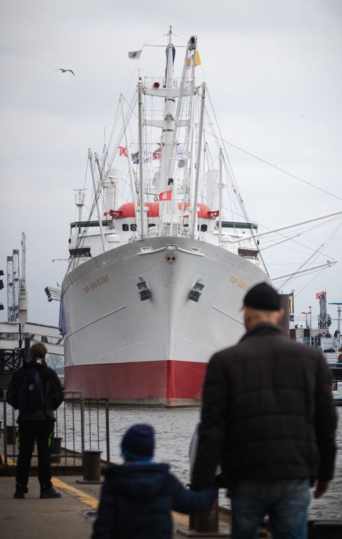 Free A large cargo ship docked at Hamburg Harbor with people enjoying the scenic view. Stock Photo