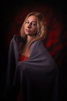 Artistic portrait of a woman draped in fabric against a dark backdrop.
