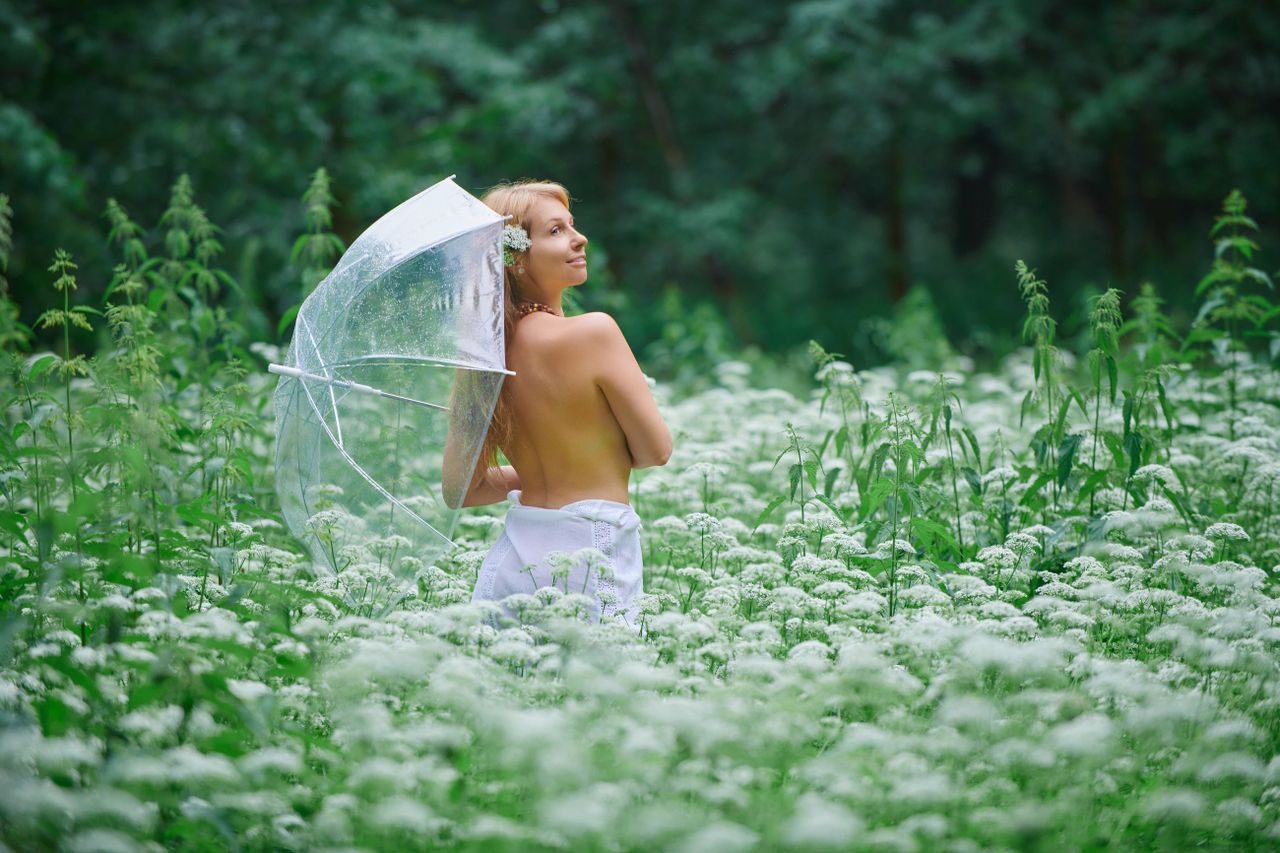 a woman in a lush field holding a clear umbrella enjoying the tranquil