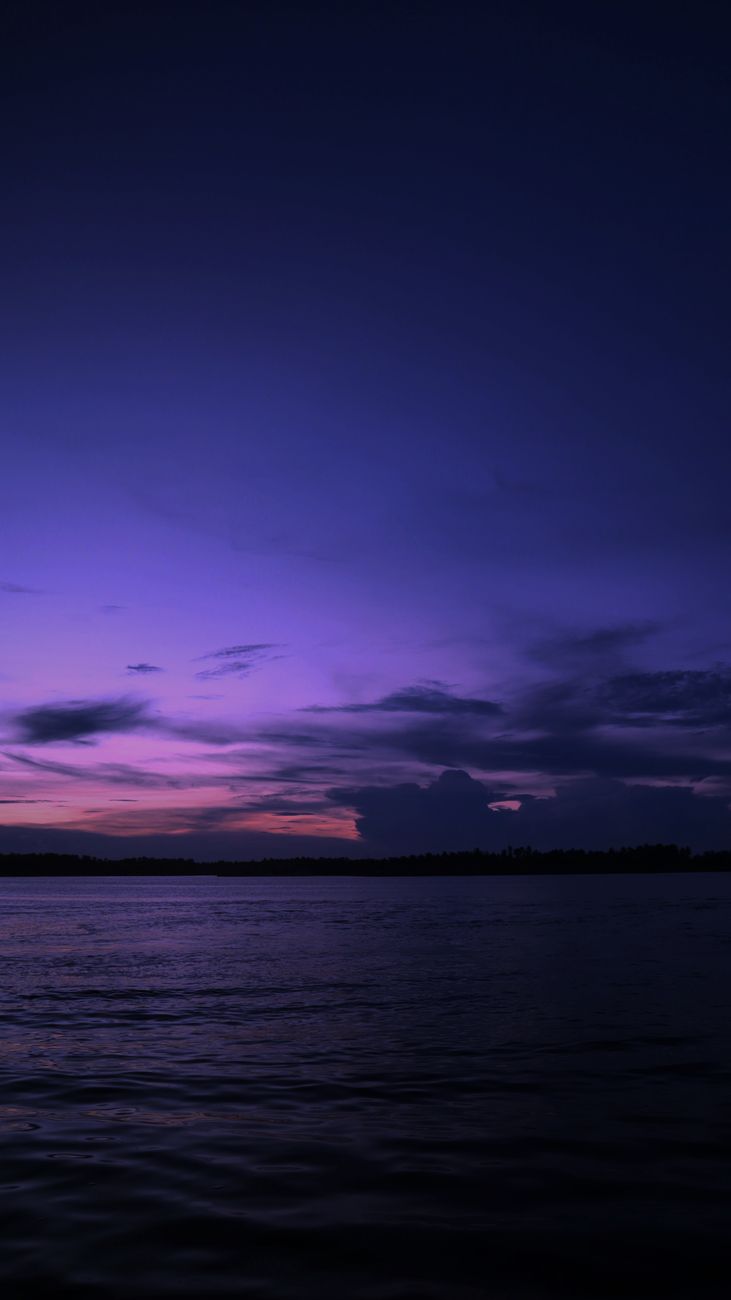 Capture of a serene ocean at twilight with vibrant purple hues and silhouetted horizon.