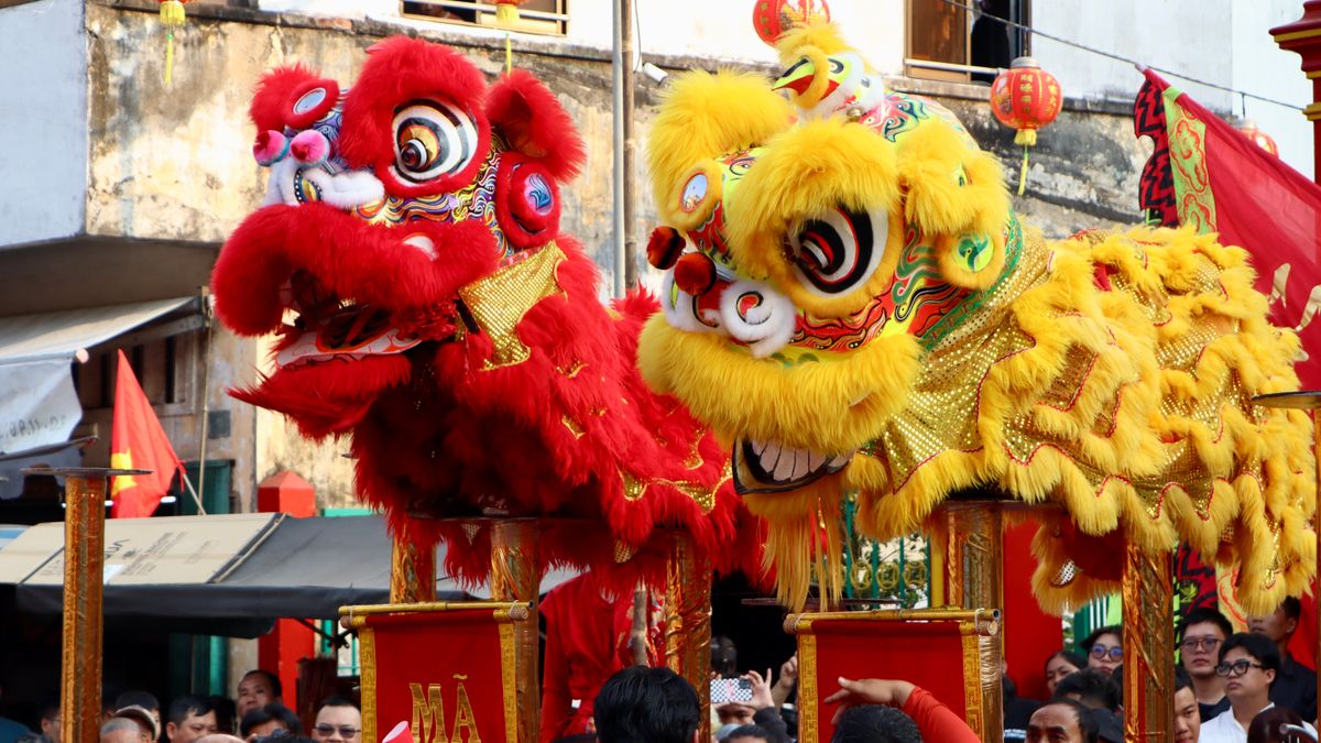 중화권 춘절 연휴 — Colorful Chinese lion dance performance amid a festive street celebration with a crowd watching.