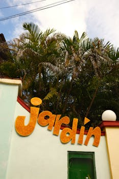Jardin sign against palm trees and colorful wall in Cuba, evoking tropical vibes.