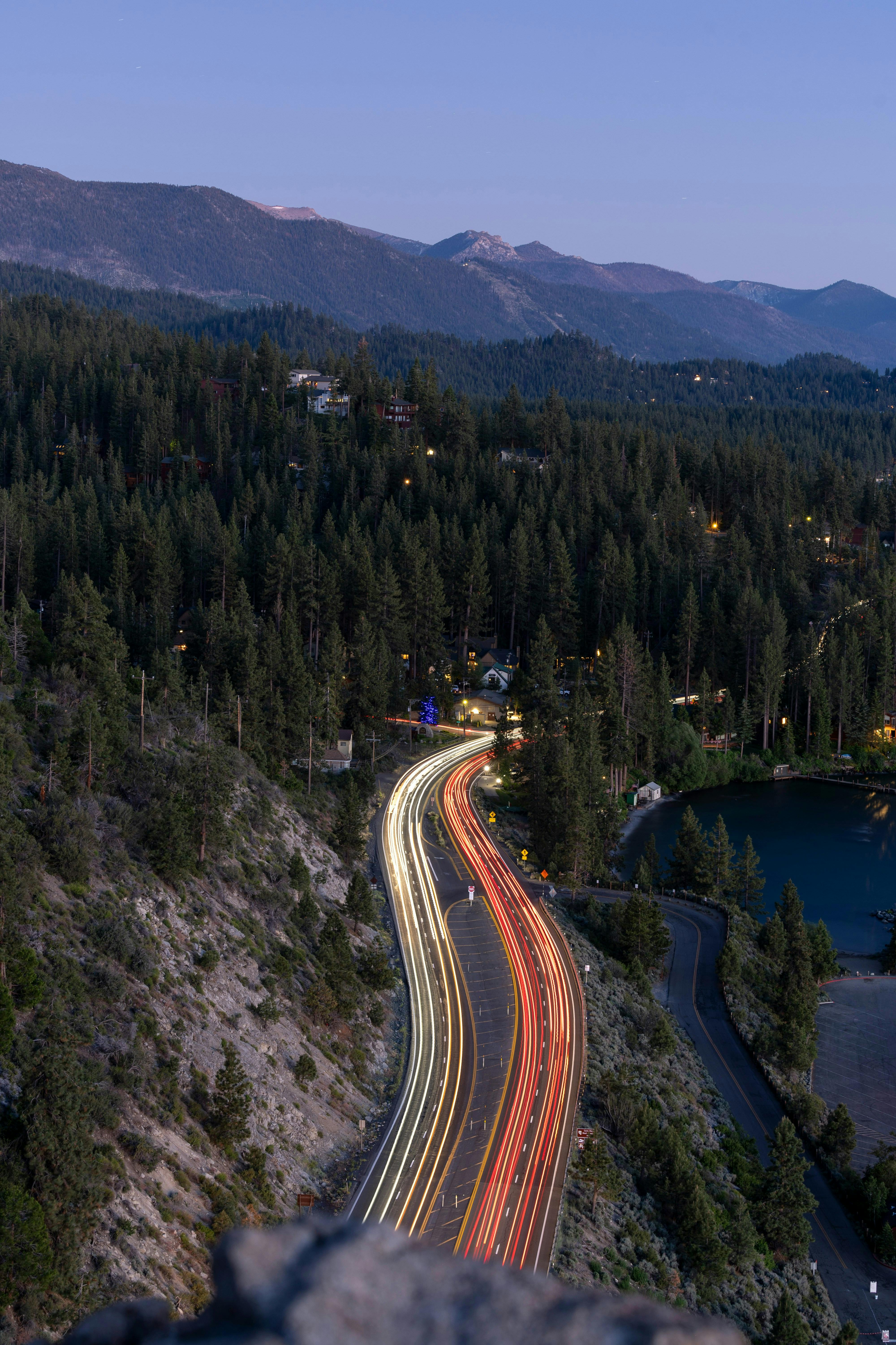 Captivating aerial shot of highway with light trails through dense forest at dusk.