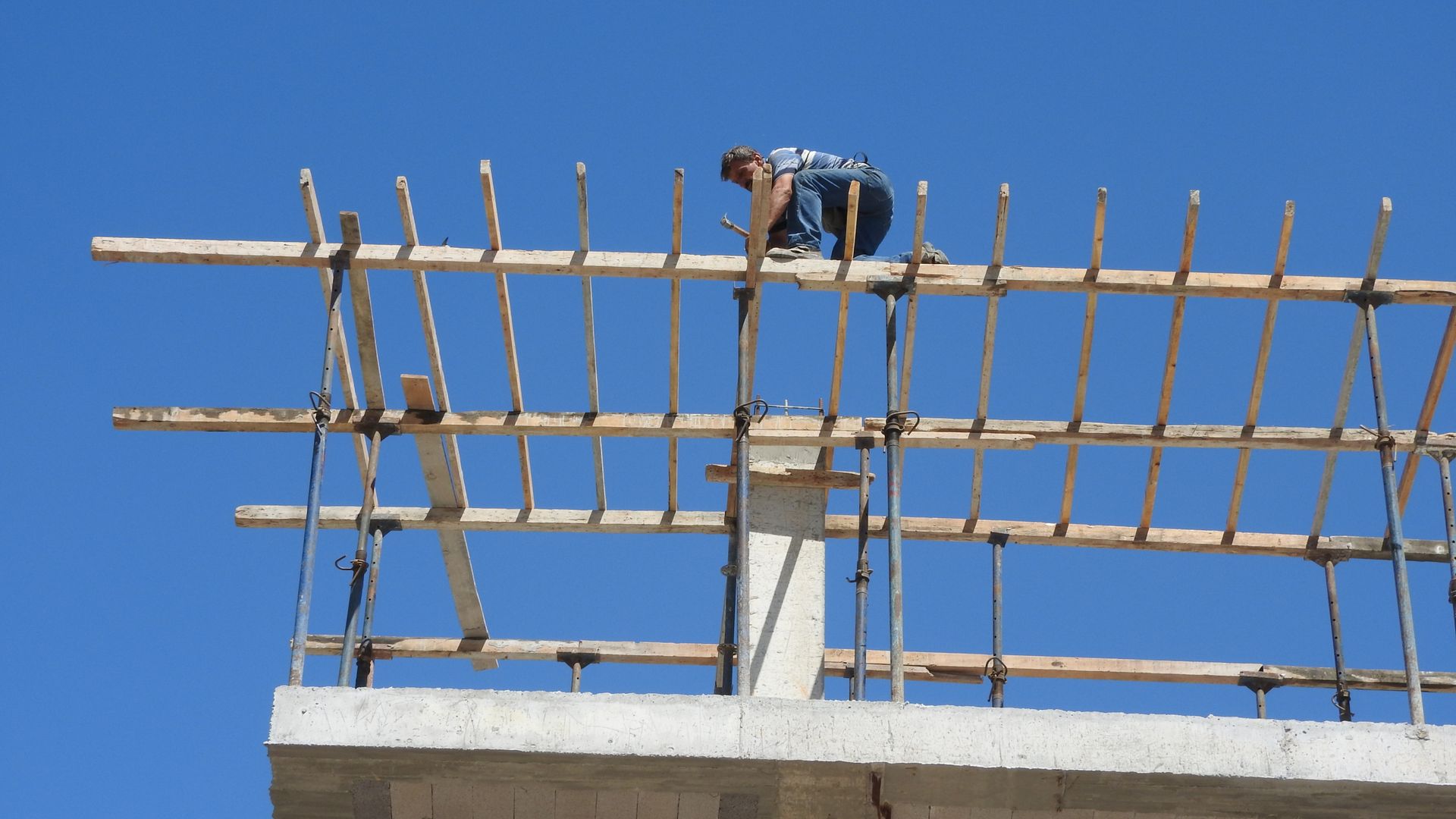 A construction worker skillfully balances on high scaffolding against a clear blue sky.