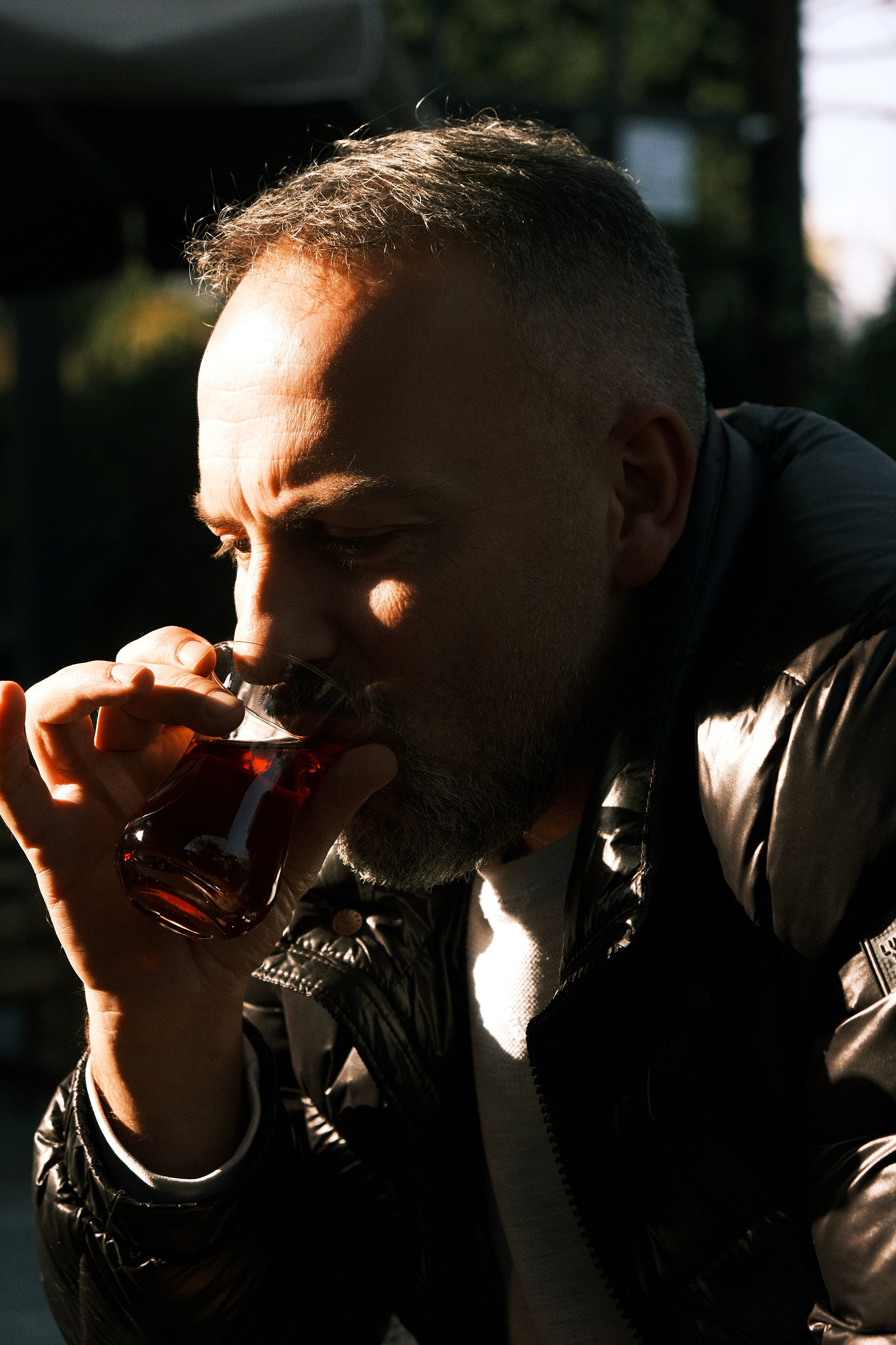 A contemplative man savors a cup of Turkish tea outdoors in sunny İstanbul, captured in natural light.
