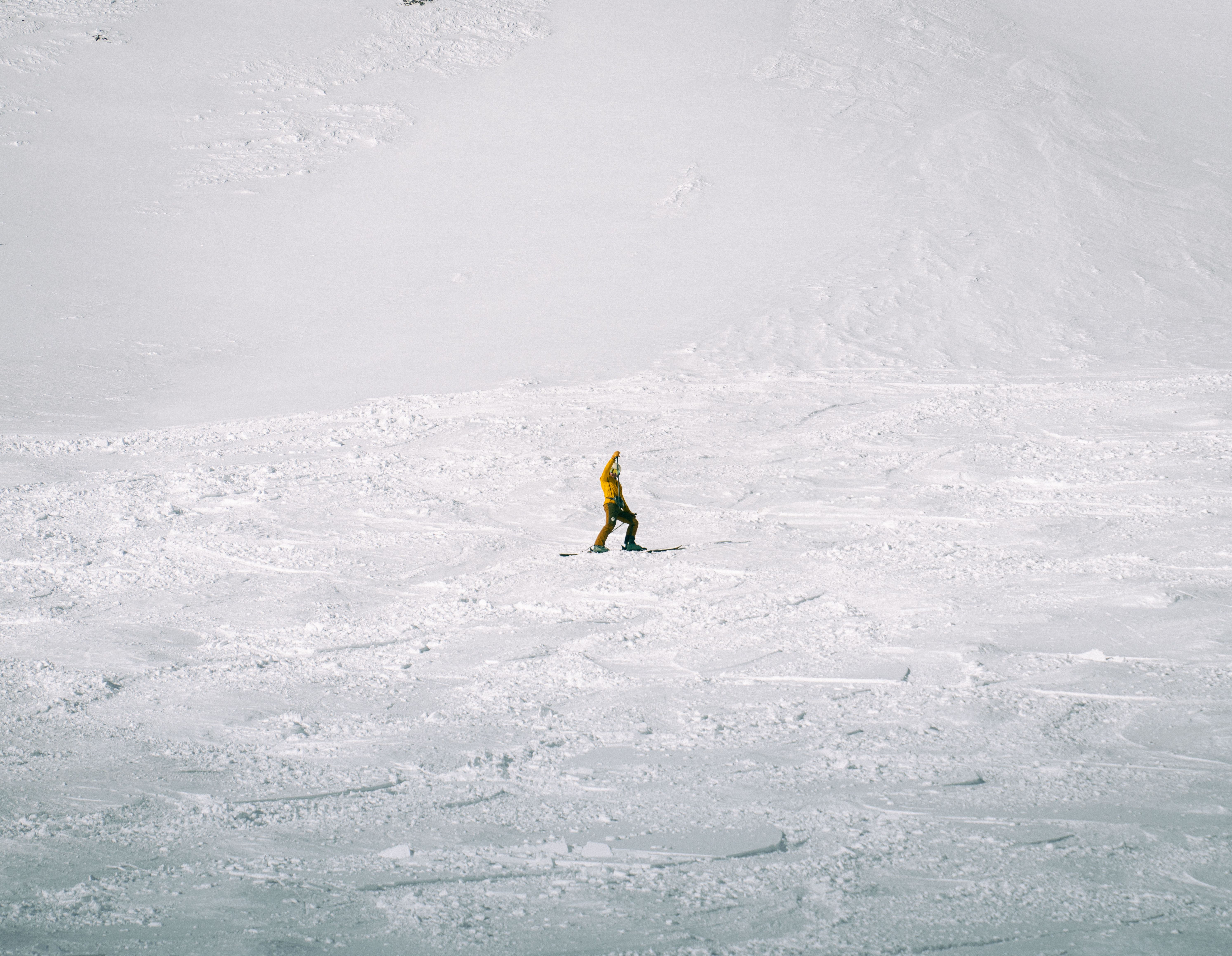 A solitary skier in a yellow jacket traverses a vast snowy mountain under a clear sky.