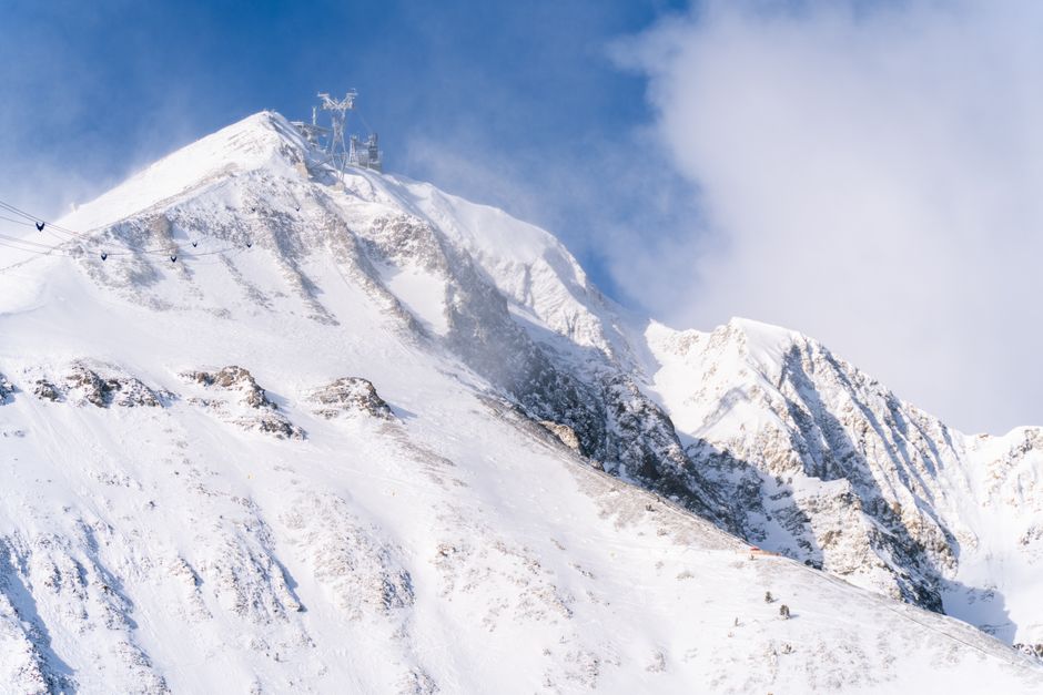 Dramatic snowy mountain peak with ski lifts under a bright blue sky, ideal for winter adventures.
